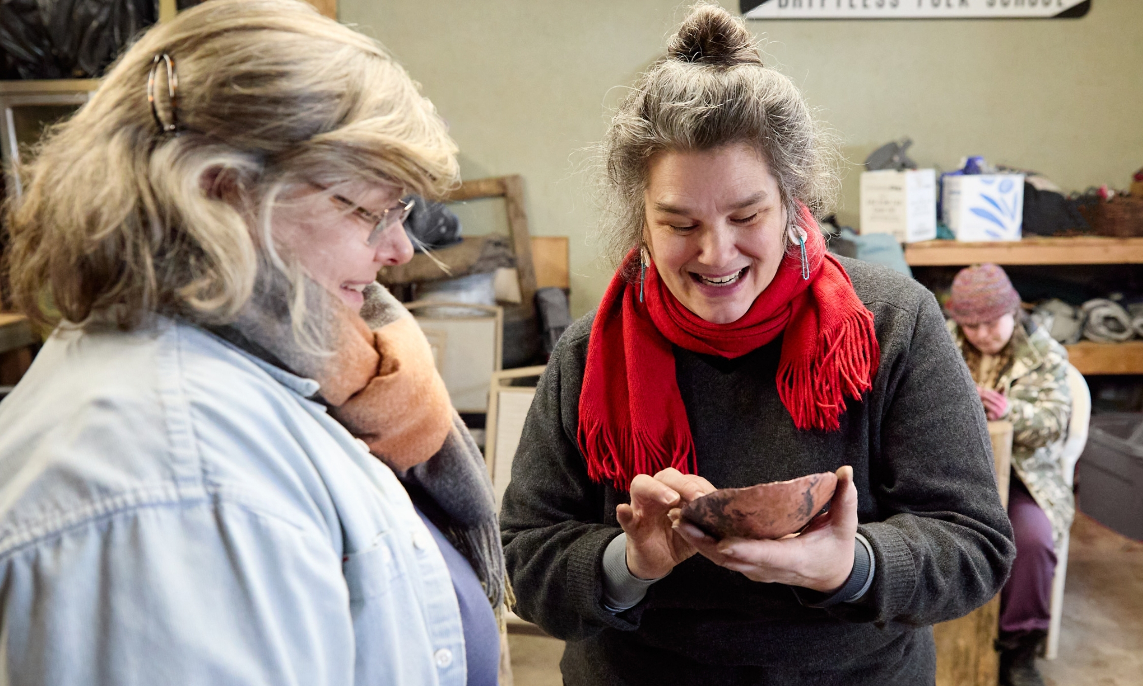 A person of medium-light skin tone with silver hair showing an adult student a copper bowl.