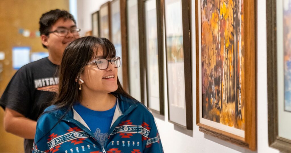 Two students smile looking at gallery art.