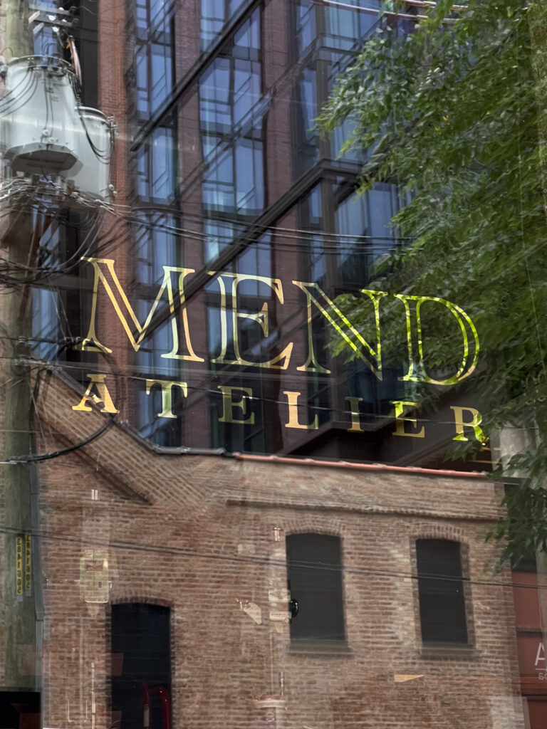 A shiny gold window sign reads: MEND ATELIER.
