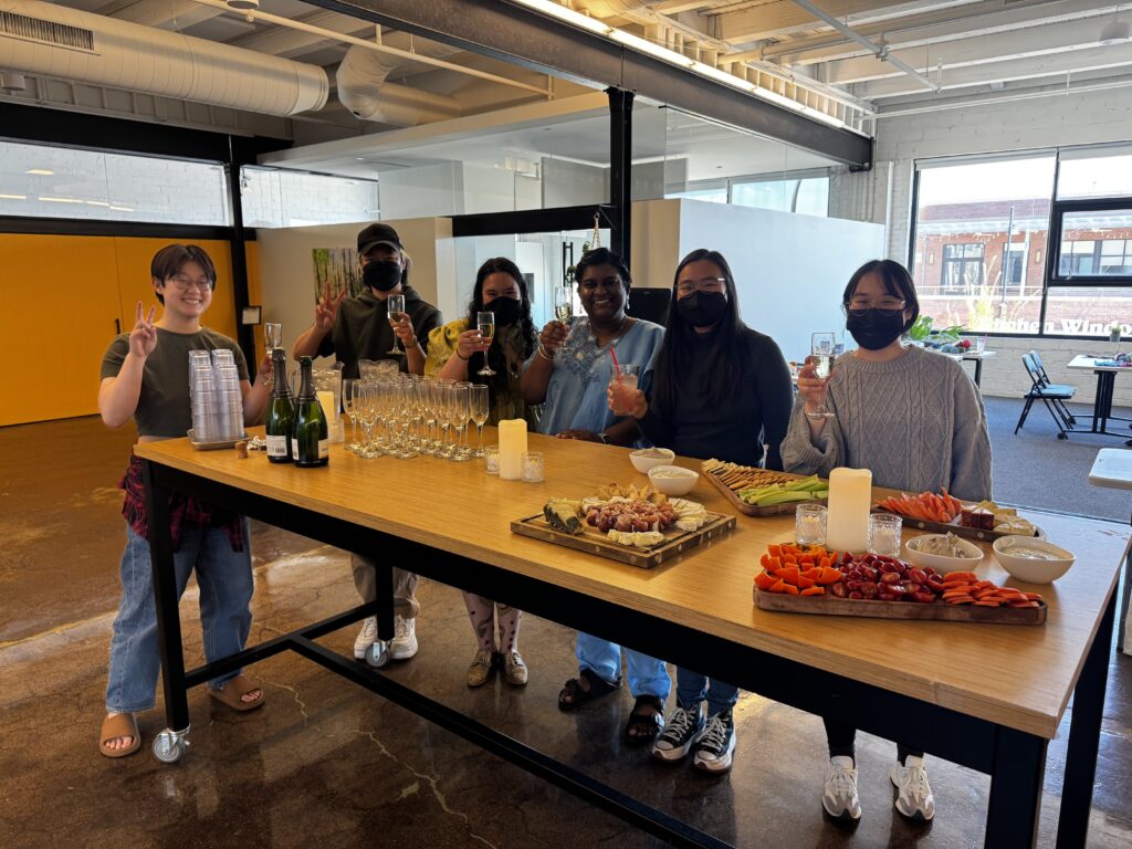 Six people holding drinks at a table with a charcuterie spread.