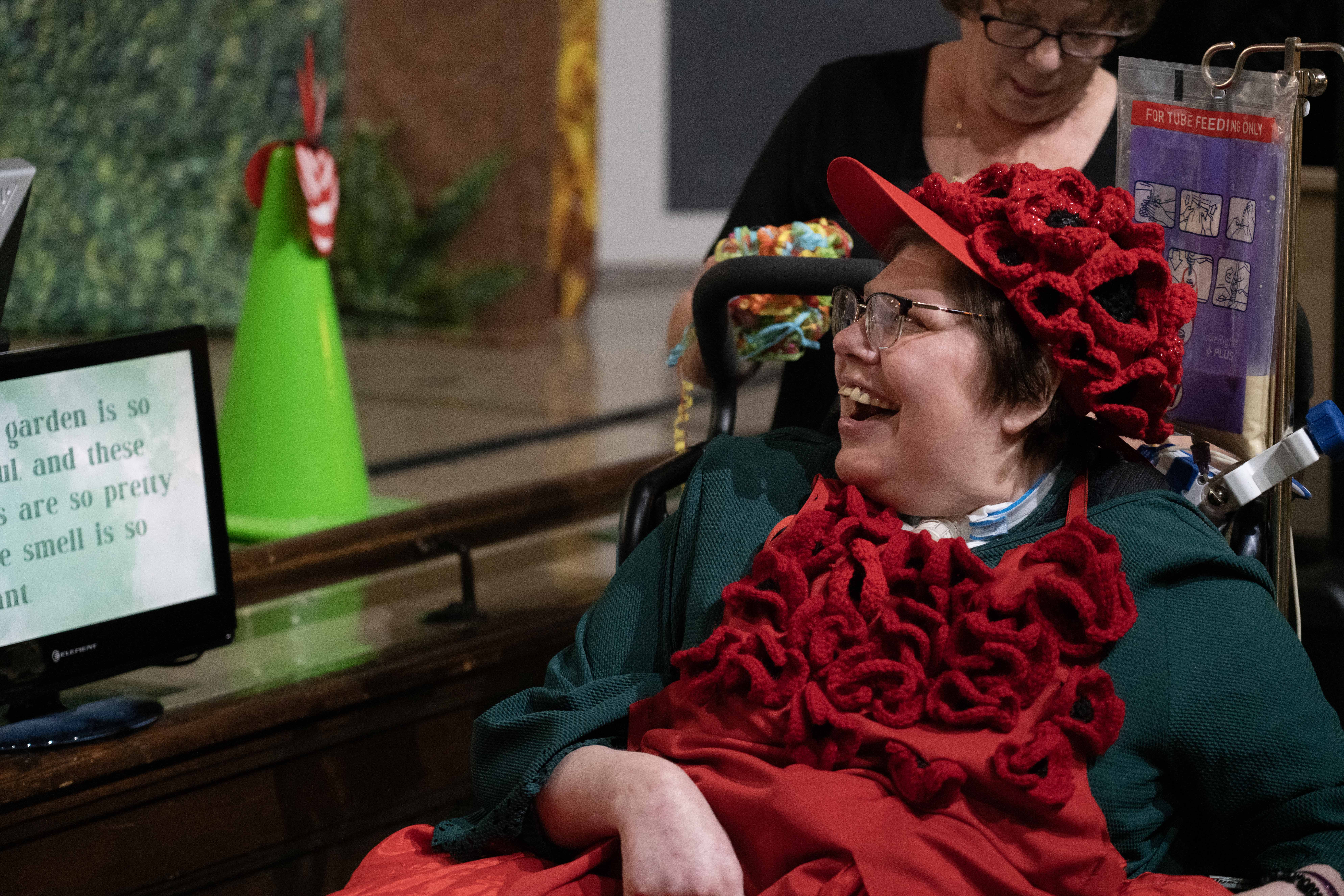 A light-skinned woman wearing red smiles and looks to her right at a screen with text on it.