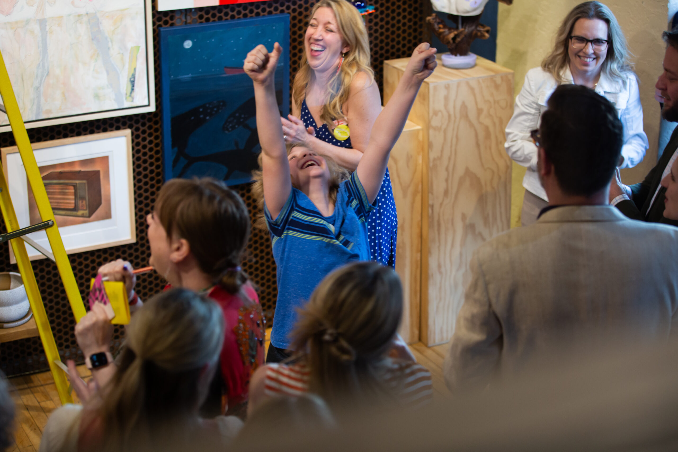 A child jumping with their arms up as adults around them smile and laugh.