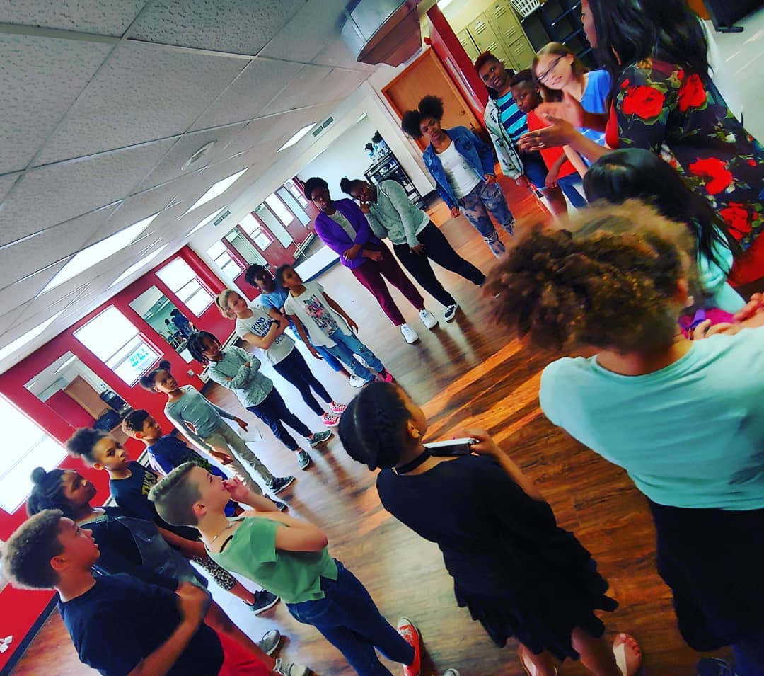 A large group of children standing in a circle listening as an adult speaks.