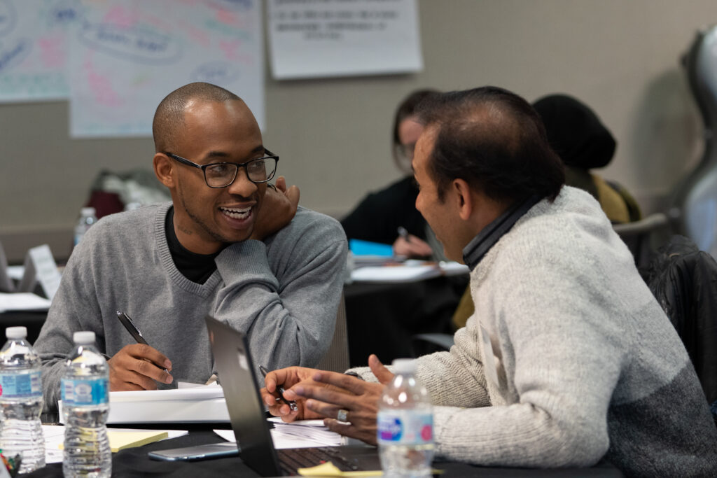 Two people sit at a table together, taking notes and talking.