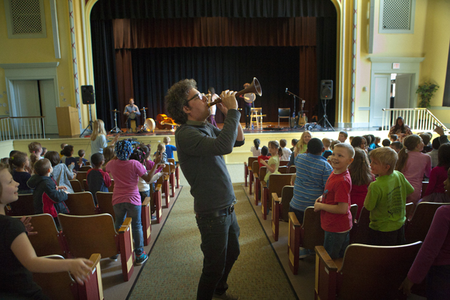 A man plays a trumpet in a school auditorium.