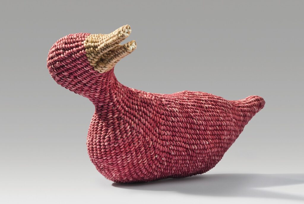 A magenta duck with yellow bill woven out of paper.