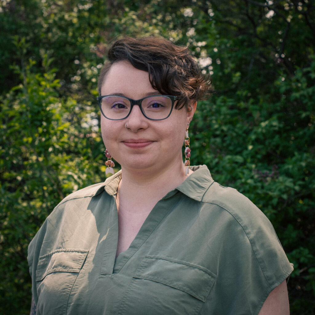 Headshot of a smiling person of light skin tone, with short brown hair pushed to one side, and wearing a sage green shirt.