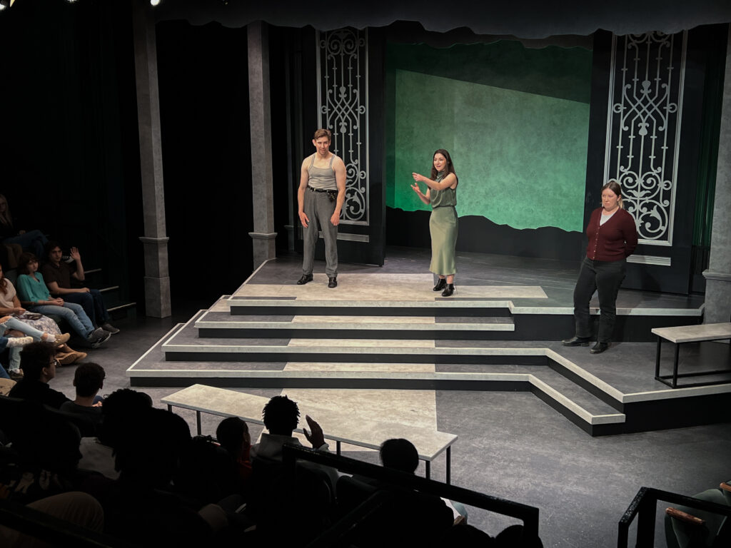 Three people standing on a thrust stage addressing an audience.