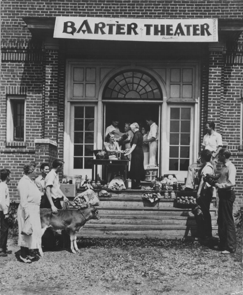 A group of people with livestock and produce outside the steps to a building with signage reading, "Barter Theater"