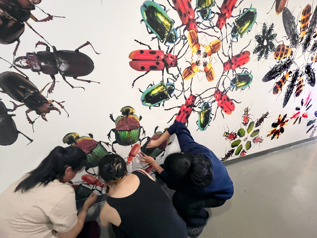 Three people working on a mural depicting colorful beetles.