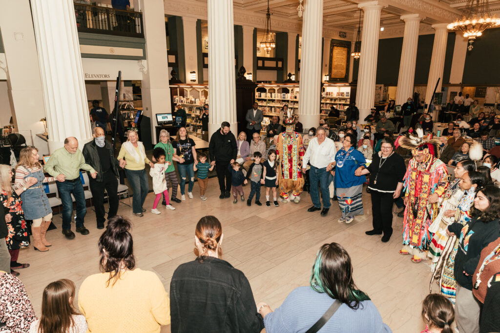 A large group of community members hold hands in a circle at Kansas City Public Library.