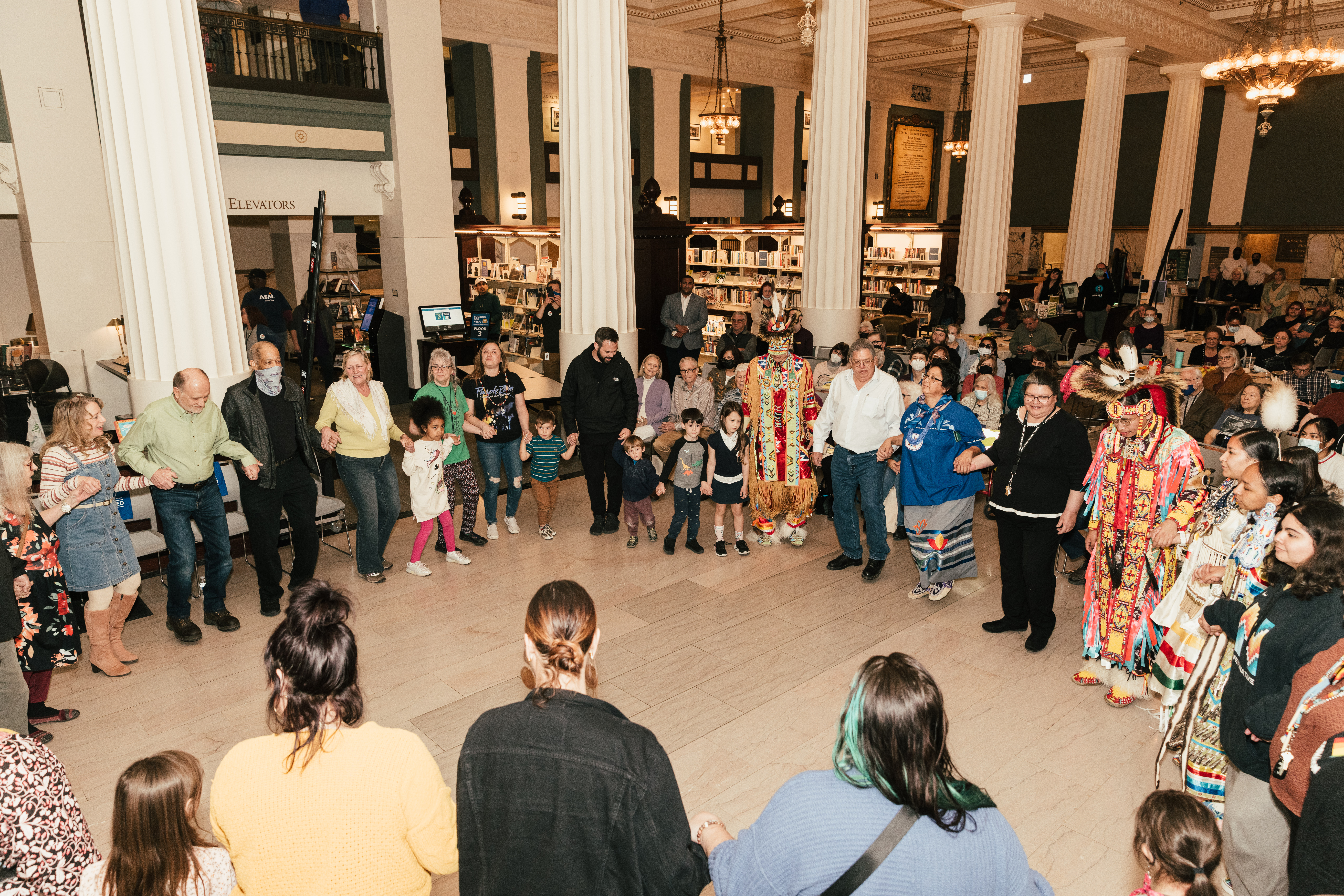 A large group of community members hold hands in a circle at Kansas City Public Library.