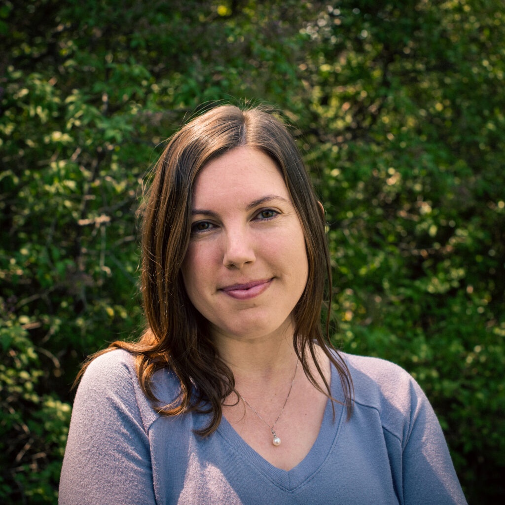 Headshot of a smiling person of light skin tone, with brown medium length hair, and wearing a purple shirt.