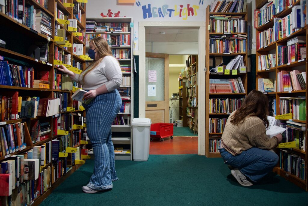 Two people searching through bookshelves on opposite ends of a room filled with books.