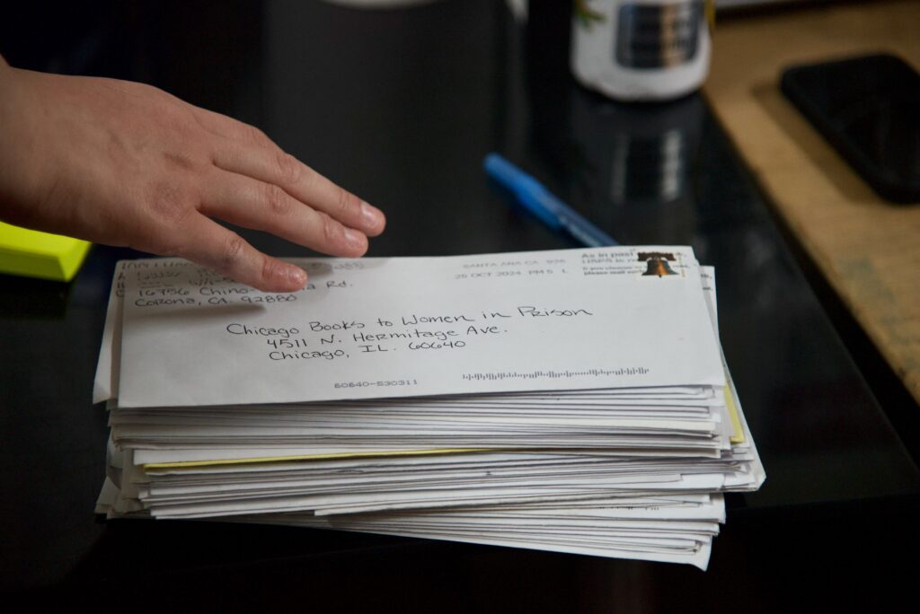 A hand reaching towards a stack of white letters addressed to Chicago Books to Women in Prison.