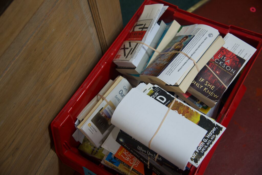 A stack of books bound with paper in a red bin sitting on the floor.