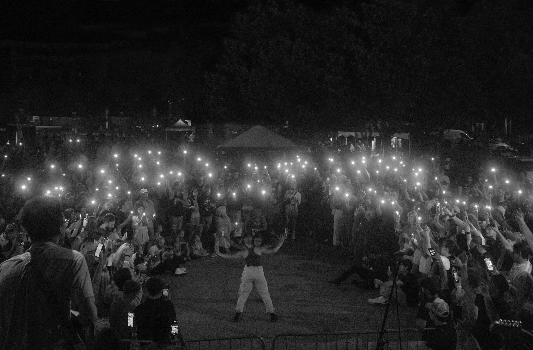 Two dancers performing at a parking lot as audience members stand around them holding up their phone flashlights.