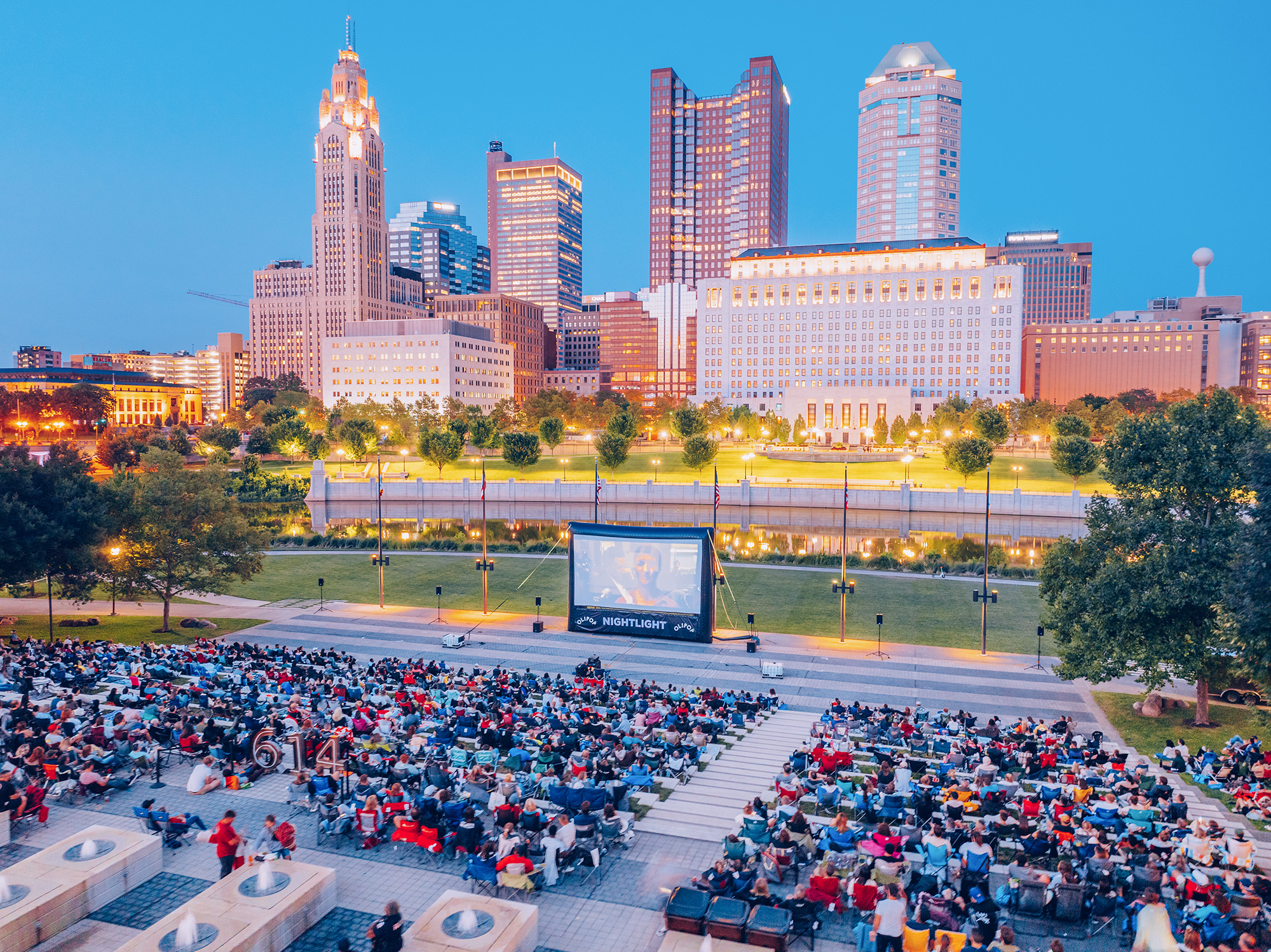 An overhead view of people sitting outdoors for a movie. There's a city skyline with tall buildings in the background.