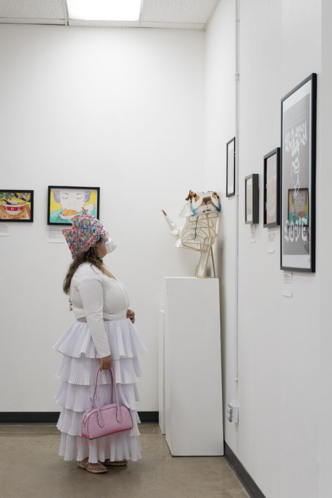 A person in a white dress looking at a piece of art on a gallery wall.