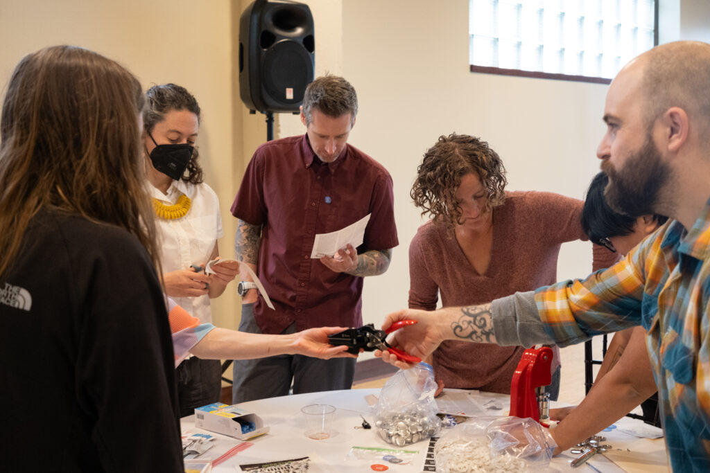Five people stand around a table using a die to cut out designs for button-making.