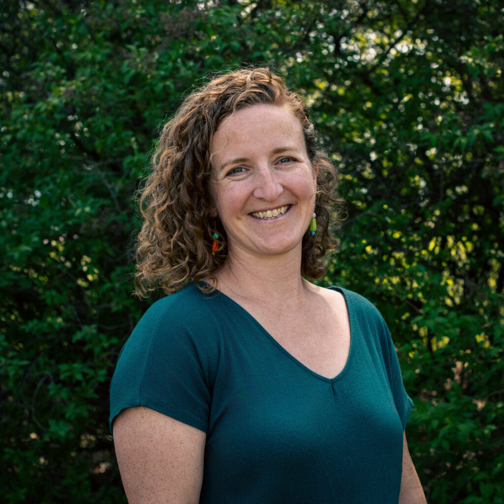 Headshot of a smiling person of light skin tone, with red short curly hair, and wearing a green shirt.