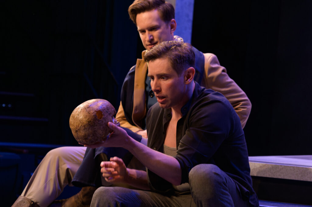 Two people sitting on stage, as one of them holds a prop skull.