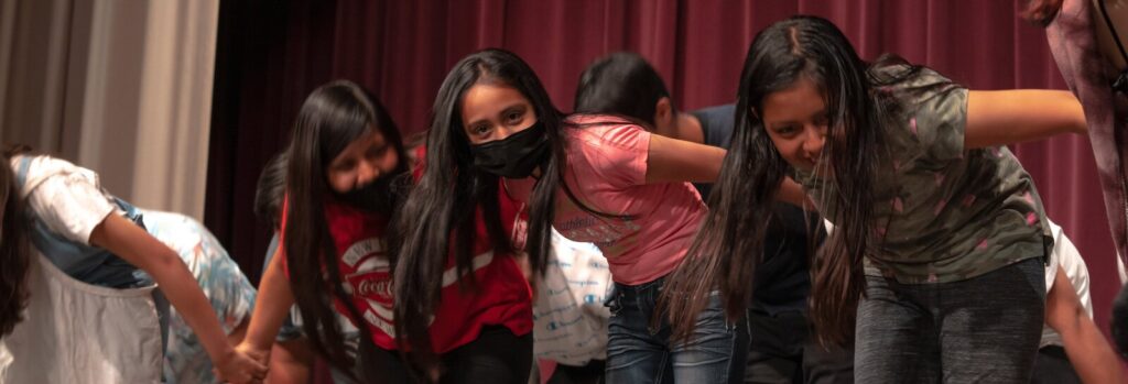 A group of young Latina teens join hands and bow on stage.