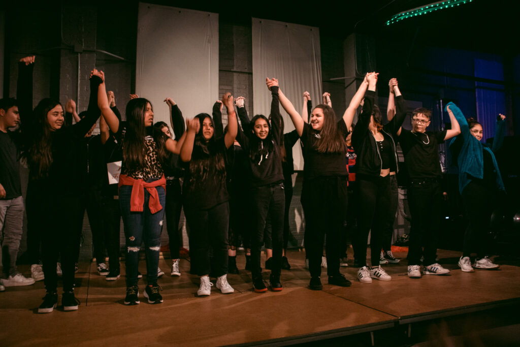 A group of teenagers hold hands to bow on stage