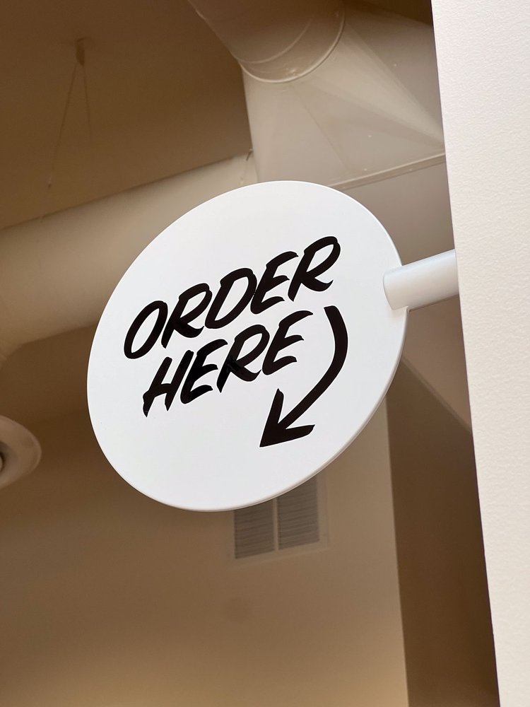 A circular white sign with black lettering reads: "ORDER HERE" with an arrow.