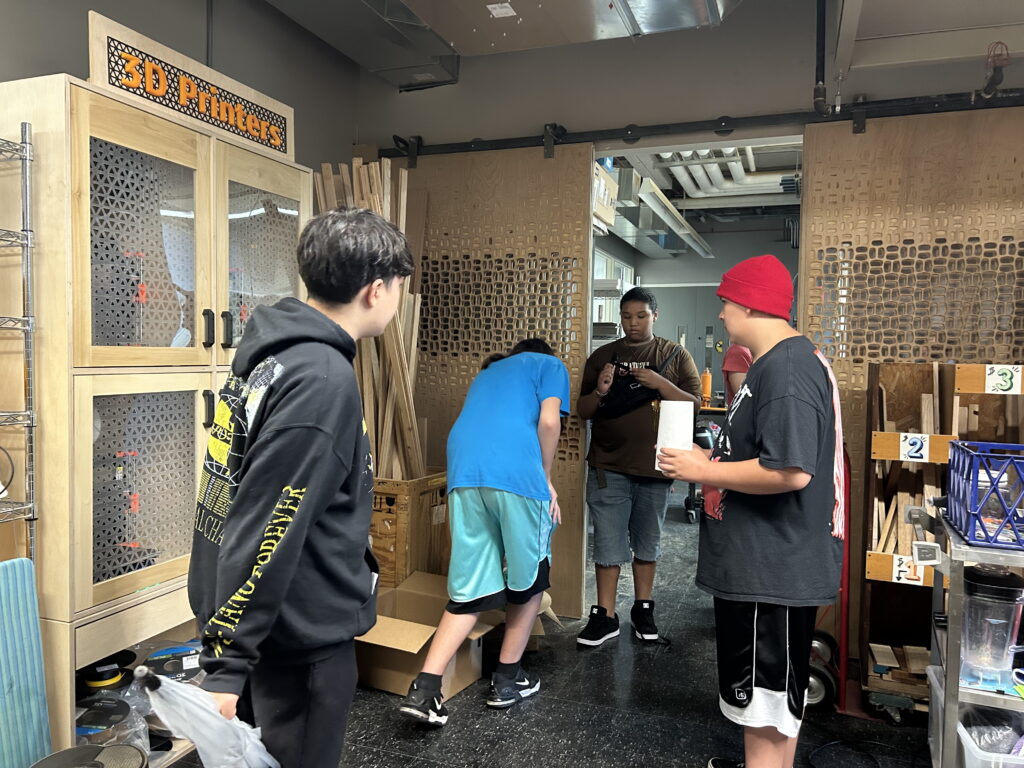 Four young people standing by a closet marked "3D Printers"