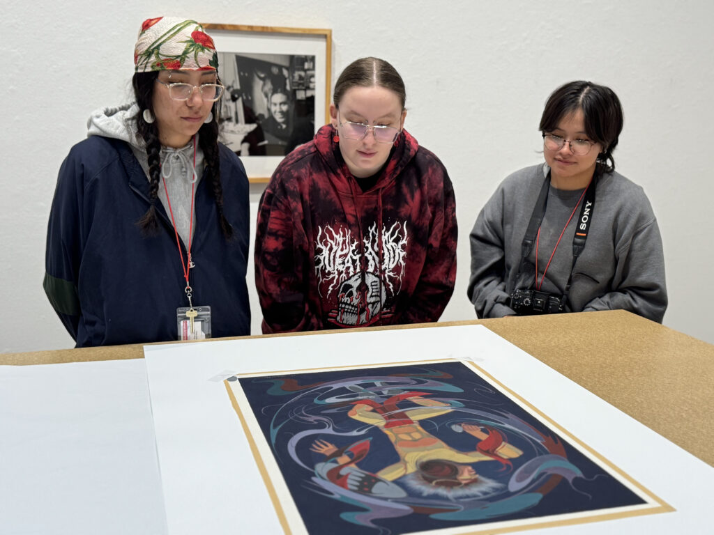 Three people look at a piece of art on a table.