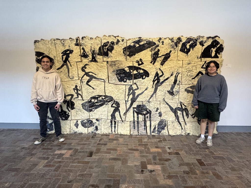 Two students stand next to an art piece