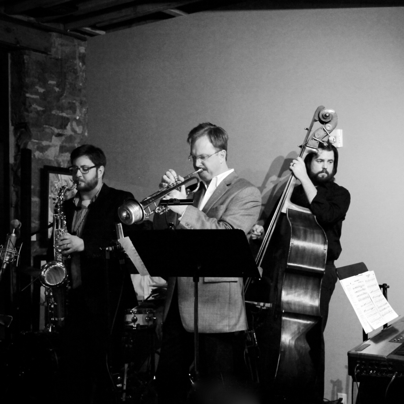 Three people playing a saxophone, trumpet, and upright bass.