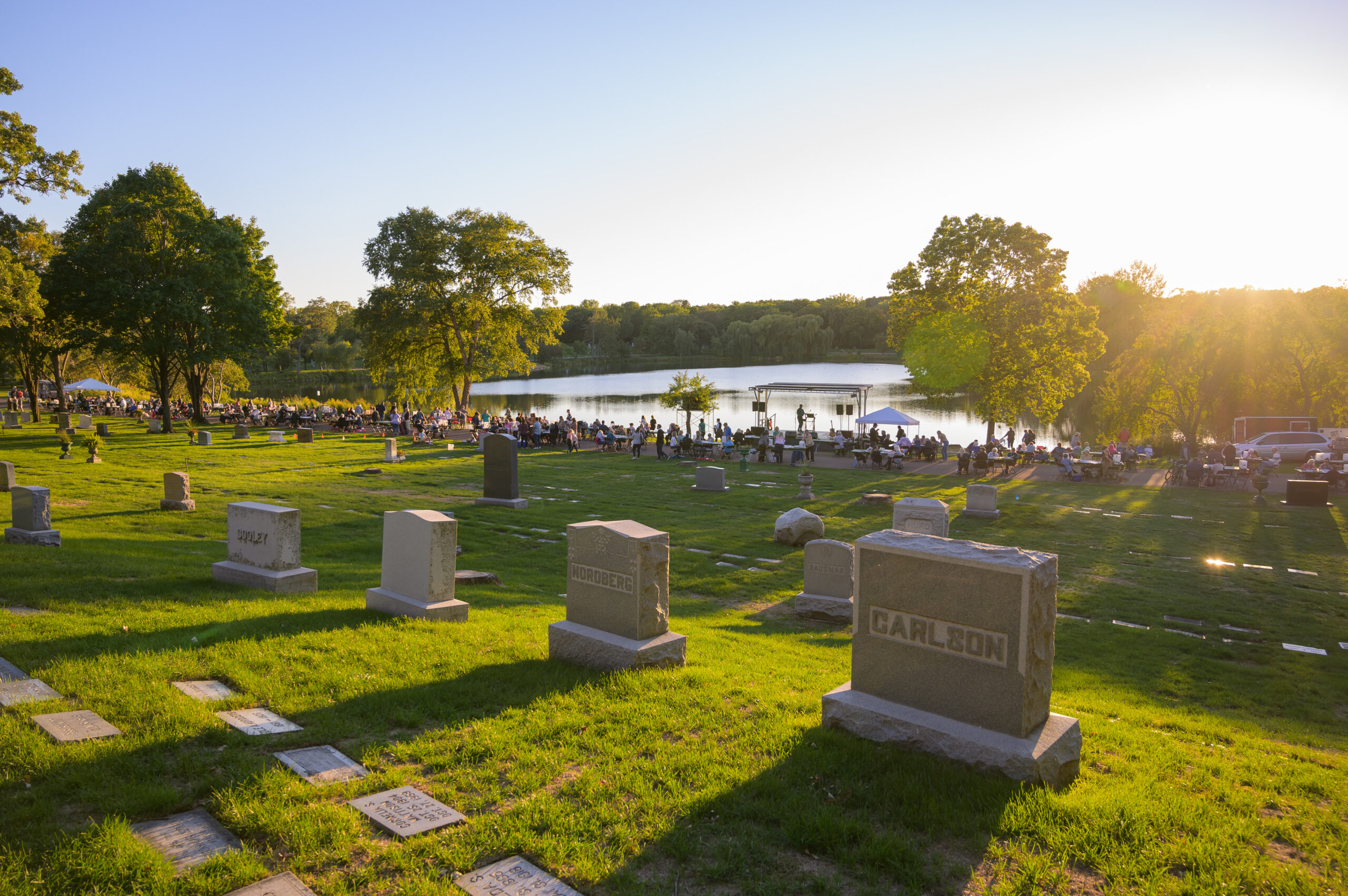 A cemetery as the sun is setting with people and a stage lining a lakeshore.