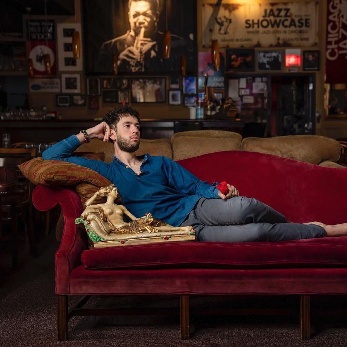 A person of light skin tone wearing a blue shirt and reclining on a red couch.
