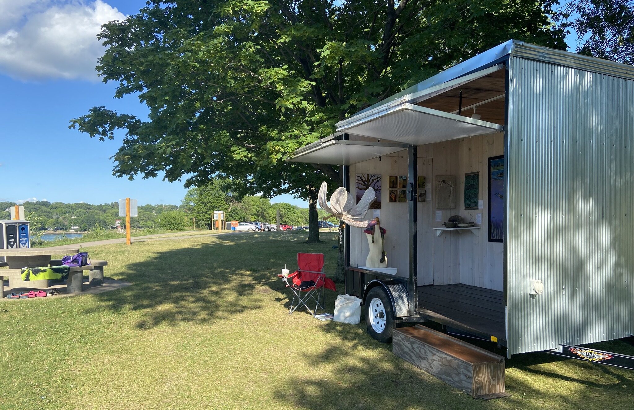 A small white trailer with art inside sits at a park.