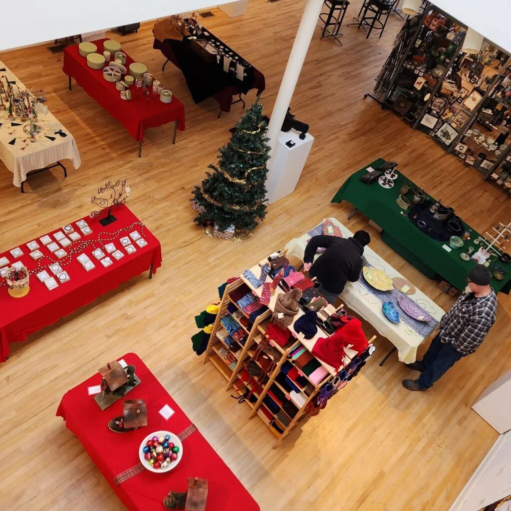 Two people browsing wares on a table at an art market.