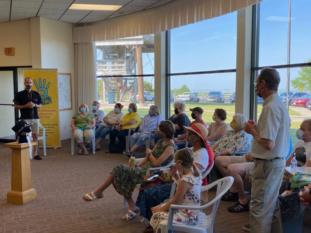 A group of people gather and sit around a speaker at an art exhibit.
