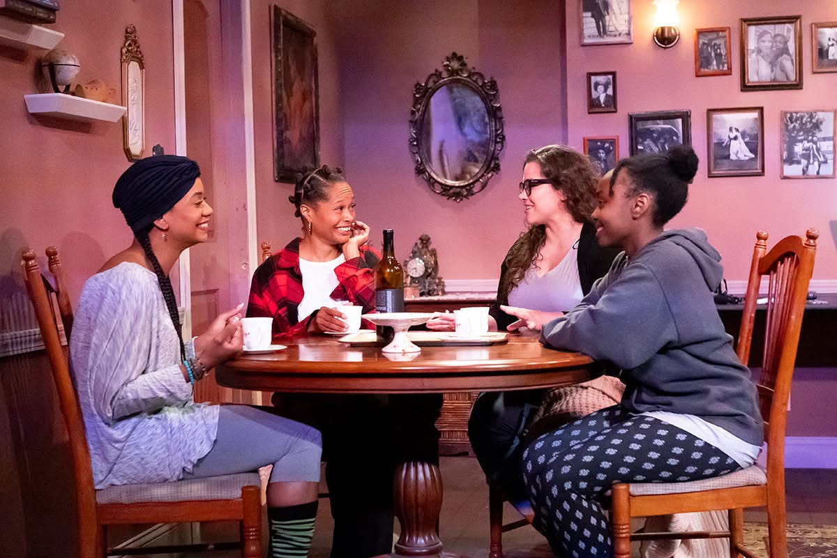 Four smiling people seated around a table drinking out of mugs.