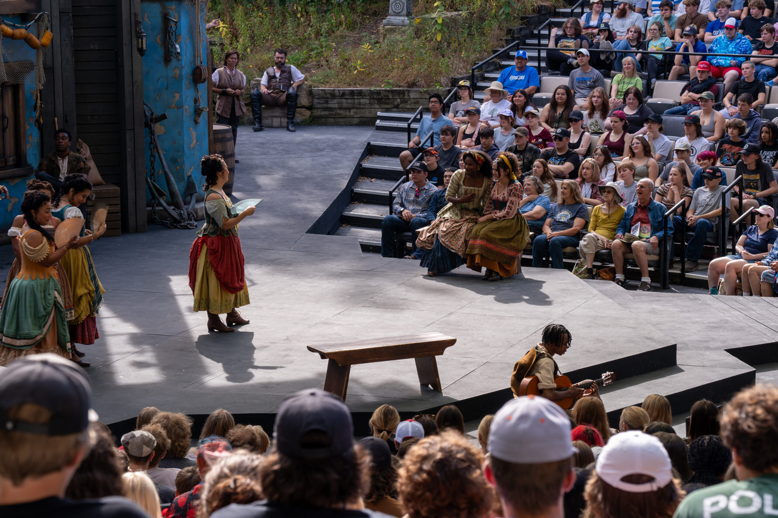 A performer on stage outdoors in front of a large audience of middle schoolers.