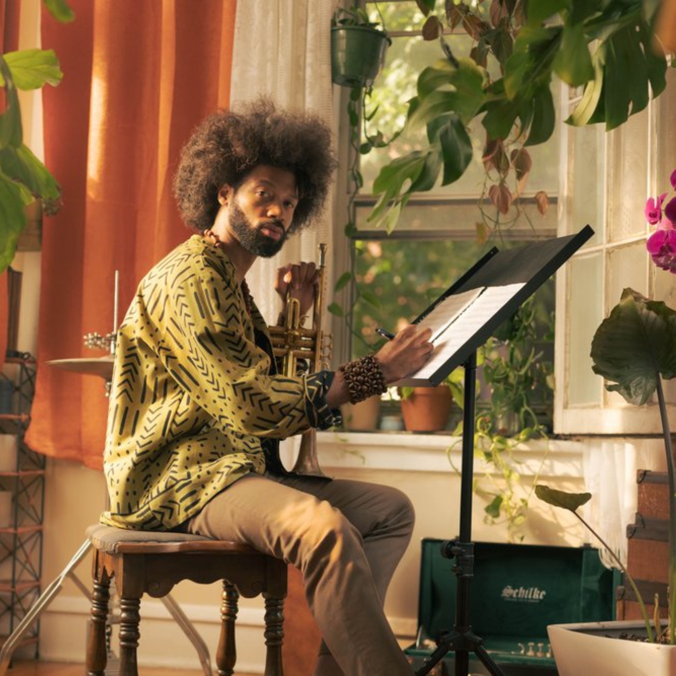 A person of dark skin tone sitting at a music stand and holding a trumpet.