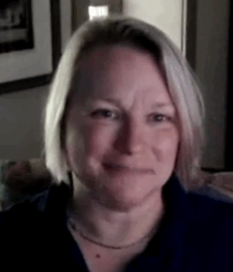 Headshot of a smiling woman with a light skin tone and shoulder length blond hair, wearing a blue polo shirt.