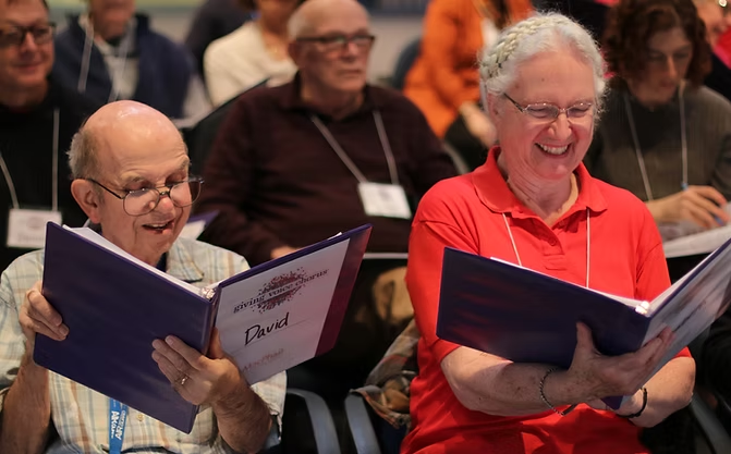 Two light-skinned people smile and hold open black binders.