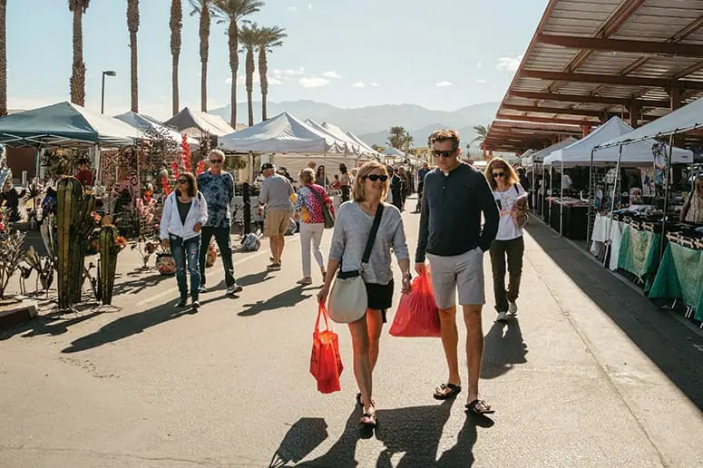 People walking through the stalls of an outdoor farmers market.